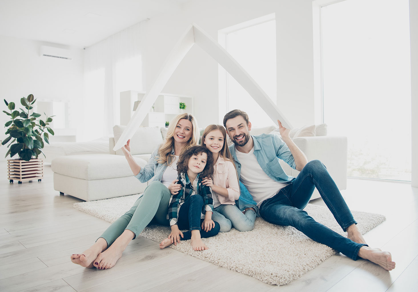 Joyful Family of Four Inside Home, Symbolically Holding a Board Above as a Roof, Representing the Security and Protection of Insurance